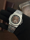 Luxury men's silver wristwatch with brown striped dial, displayed on a gloved hand
