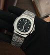 Luxury stainless steel men's watch with black dial held by gloved hand, modern design
