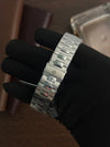 Luxury stainless steel men’s watch bracelet with clasp, held by gloved hand, on wood background