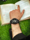 Man wearing a modern black men’s watch while reading a book on green grass